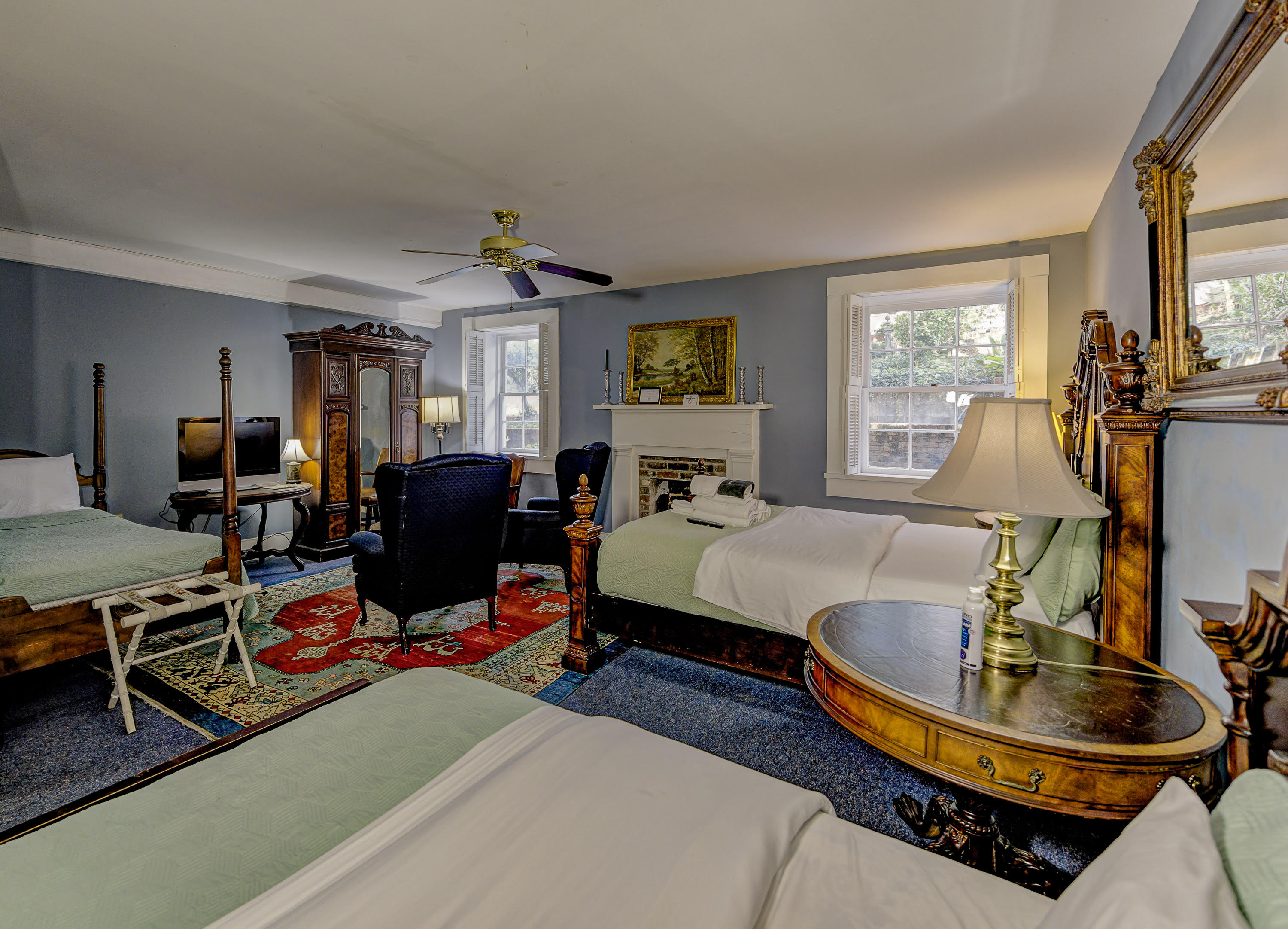 two doube beds with end tables and lamps, white mantle, oriental rug, blue wing chair