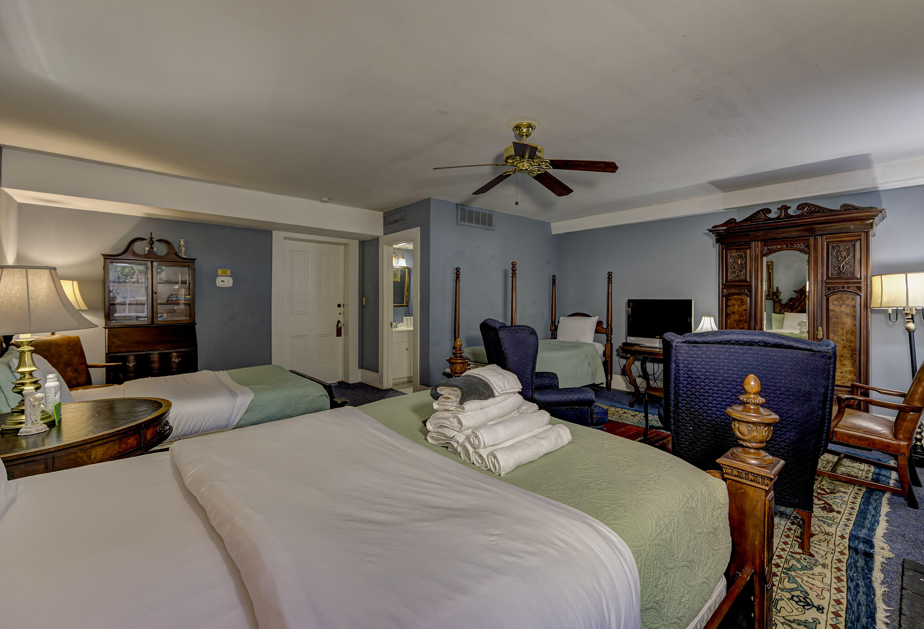 windows with shutters, ceiling fan, two blue wing chairs, table between oriental rug, lamps