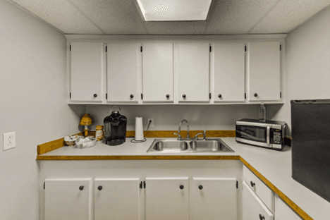 small kitchenette, white cabinets, counter refrigerator, microwave, coffee maker