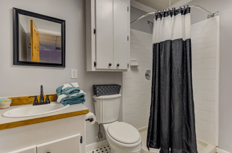 single vanity, toilet with cabinet over, stand up shower with black and white shower curtain.