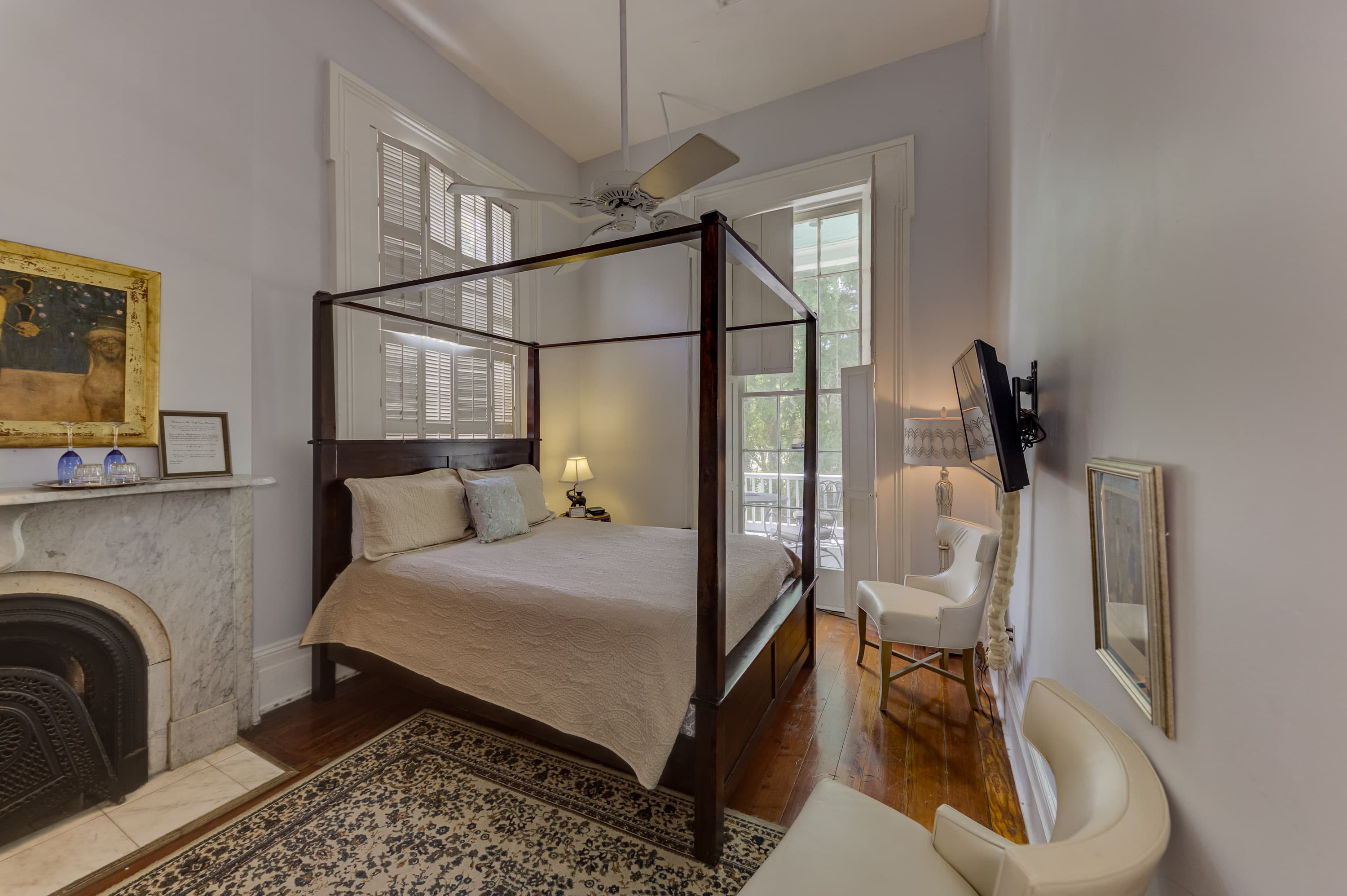 Four poster bed, one of only two original Italian marble fireplaces, tall windows with shutters, two small white leather chairs.