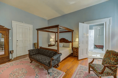 grey walls, one multi colored chair, black sofa, king four poster bed