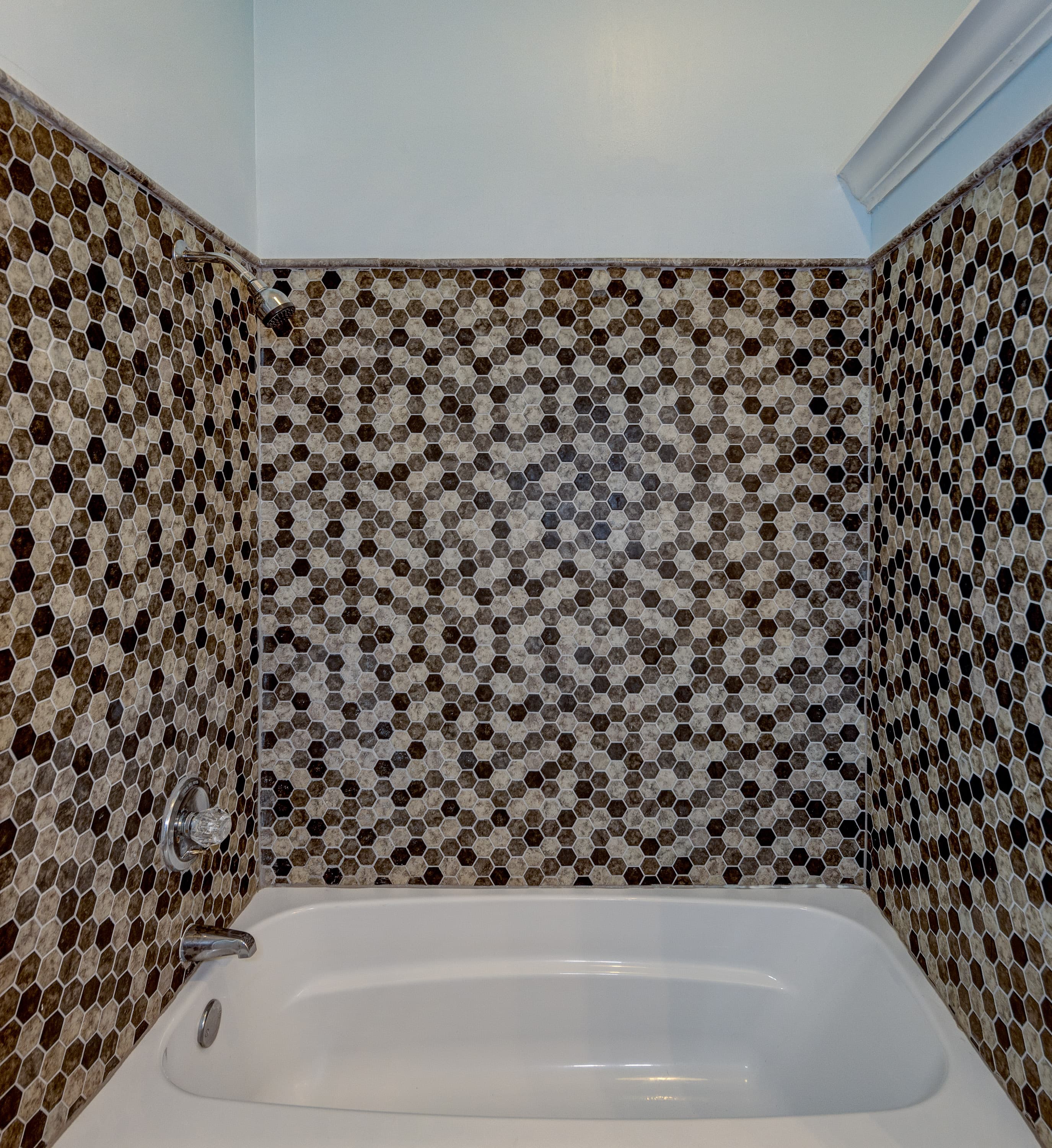 close up of white tub, multi colored brown surround shower, molding at top