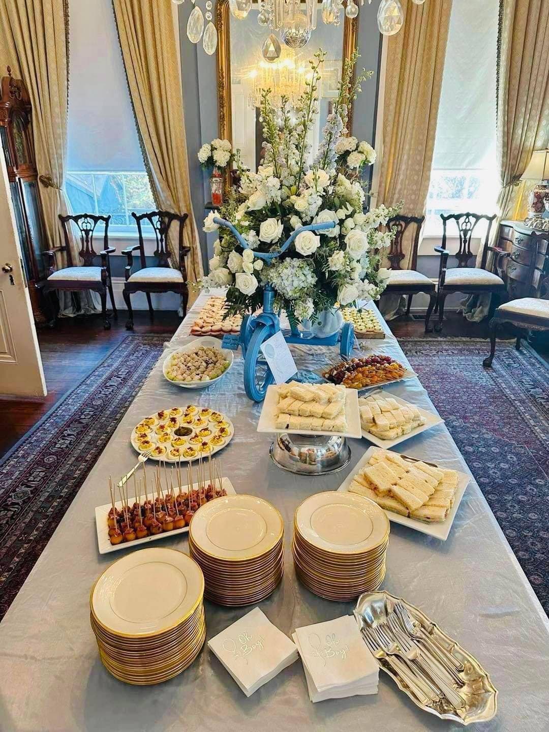 A beautifully arranged table covered with a variety of appetizers and desserts, featuring a floral centerpiece and elegant tableware.