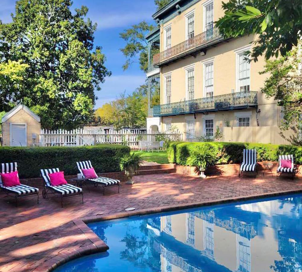 A tranquil pool area featuring striped lounge chairs and lush landscaping in front of a historic building.