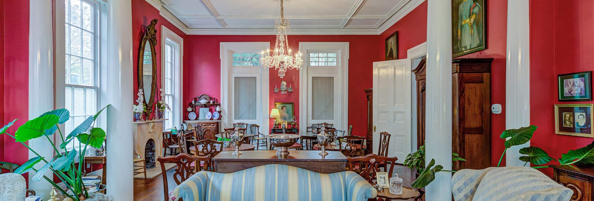 A elegantly decorated room featuring red walls, antique furniture, and a chandelier.