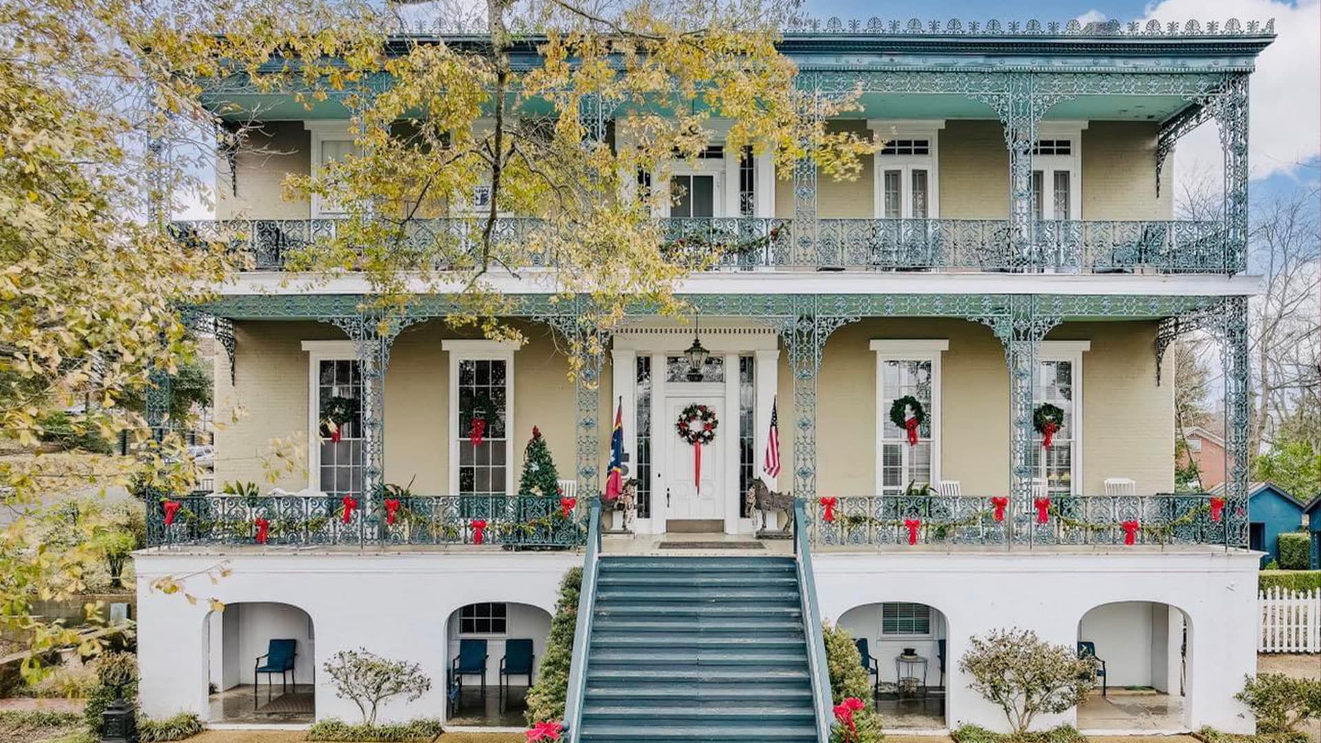 A beautifully decorated historic house with festive wreaths and garlands, featuring a grand staircase and balconies.