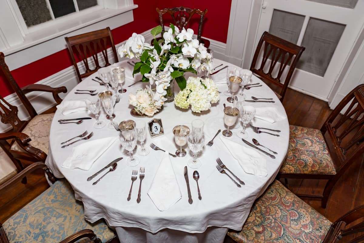 An elegantly set dining table with a floral centerpiece on a white tablecloth.