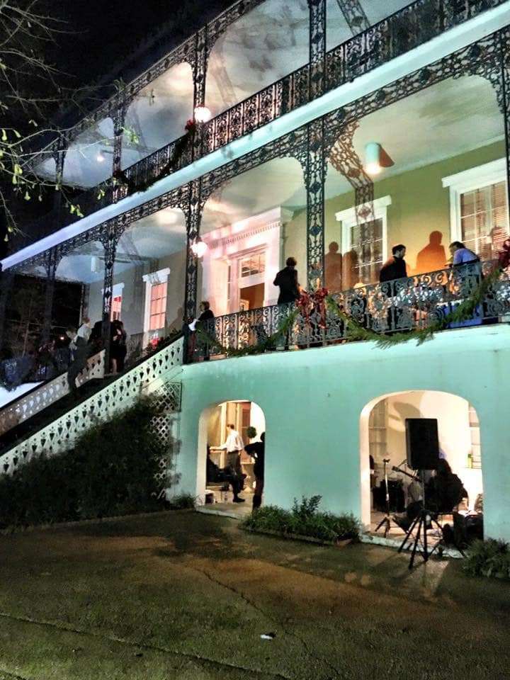 A beautifully lit historic building with intricate ironwork and people socializing on its balcony at night.