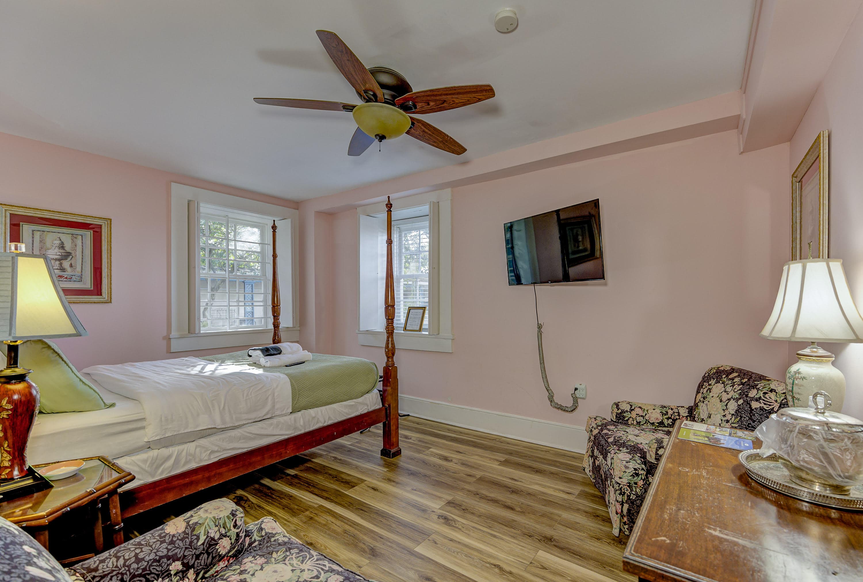 A cozy pink bedroom featuring a four-poster bed, a TV, and two floral armchairs.