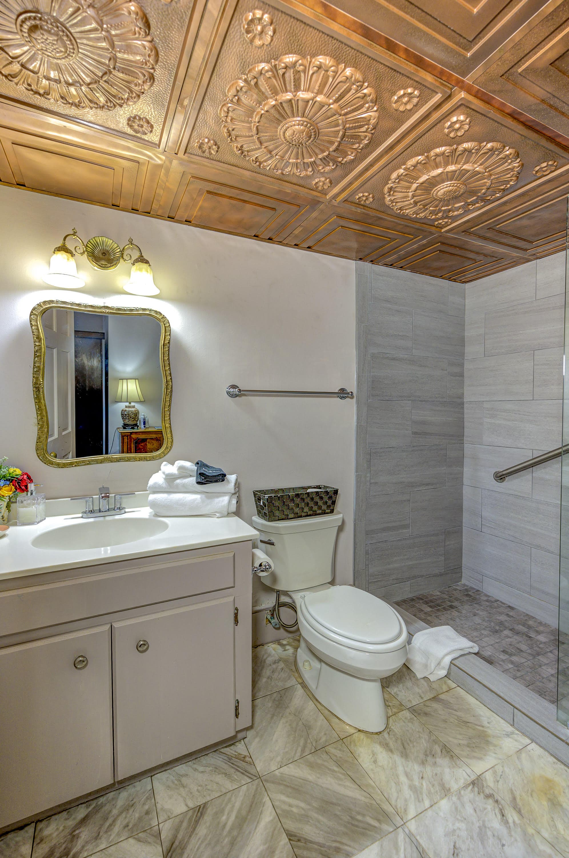 A well-decorated bathroom featuring a mirror, sink, toilet, and glass-enclosed shower with decorative tiles.