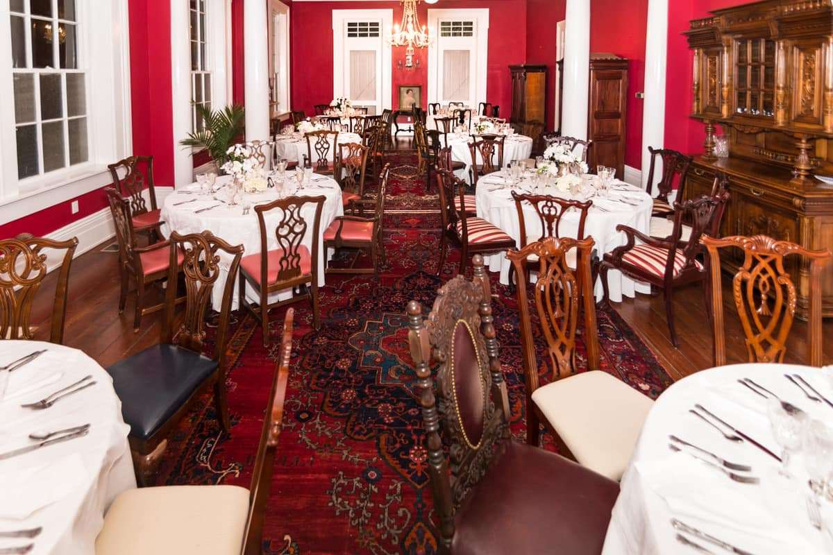 Elegant dining room with round tables set for a meal, adorned with white tablecloths and floral centerpieces, against a red wall backdrop.