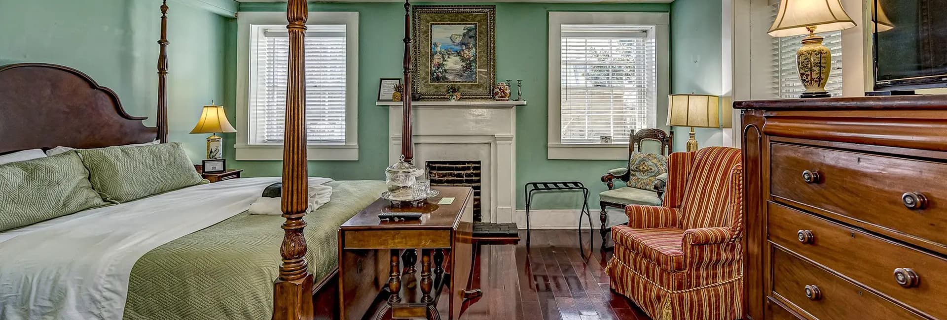 A cozy bedroom featuring a four-poster bed, wooden furniture, and green walls.