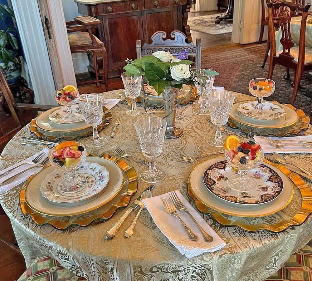 A beautifully set dining table with floral centerpieces and dessert cups, surrounded by ornate dishware and elegant glassware.