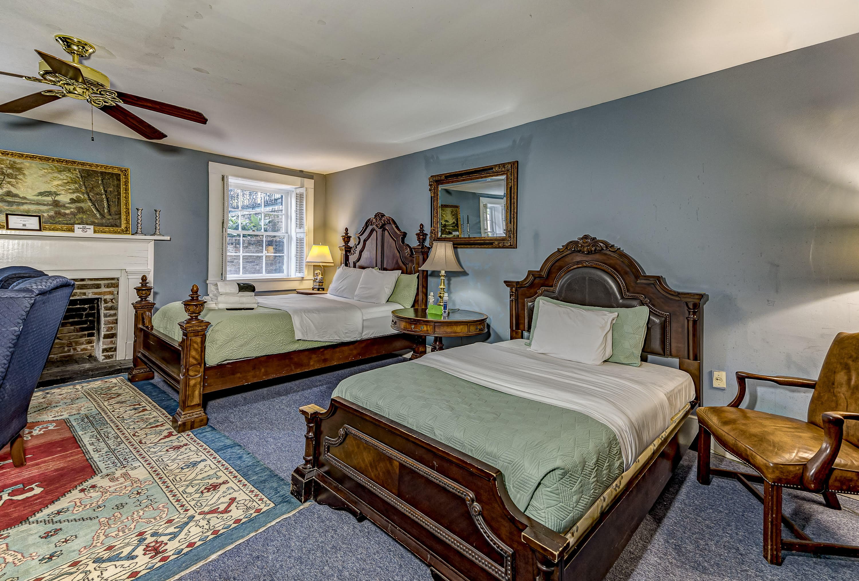 A cozy bedroom featuring two antique wooden beds with green bedding, a fireplace, and a mirrored dresser.