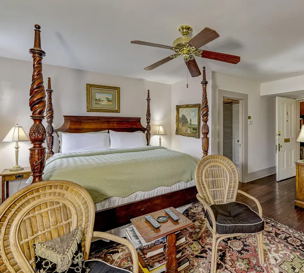 Cozy bedroom featuring a four-poster bed, wicker chairs, and decorative artwork.