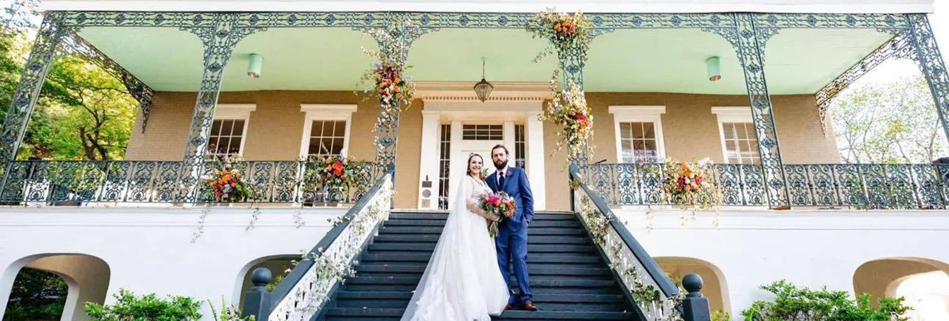 A bride and groom stand on the staircase of a beautifully decorated historic building.