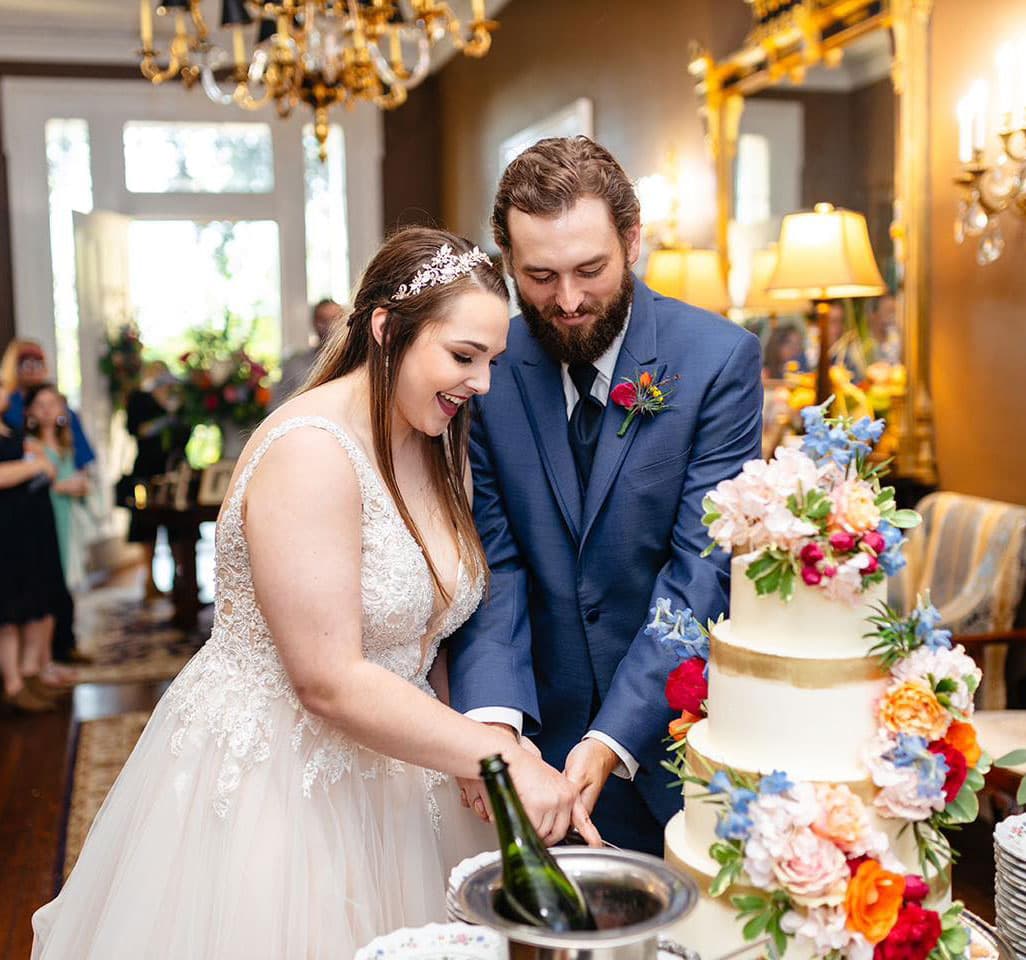 A bride and groom joyfully cut their wedding cake surrounded by decor and guests.