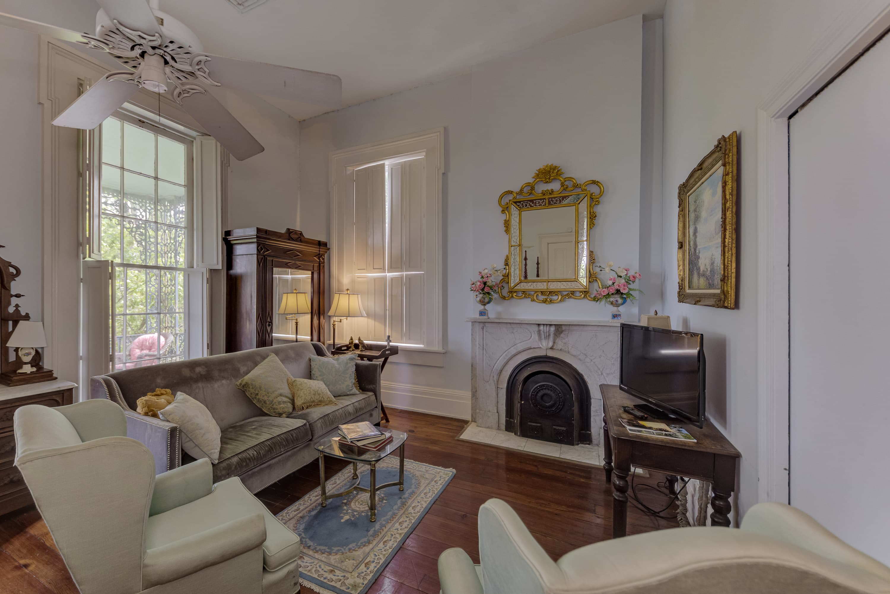 15.5 foot ceiling, Italian Marble mantle with gold mirror over, grey sofa, two green wing chairs, armoir, ceiling fan, floor to ceiling windows