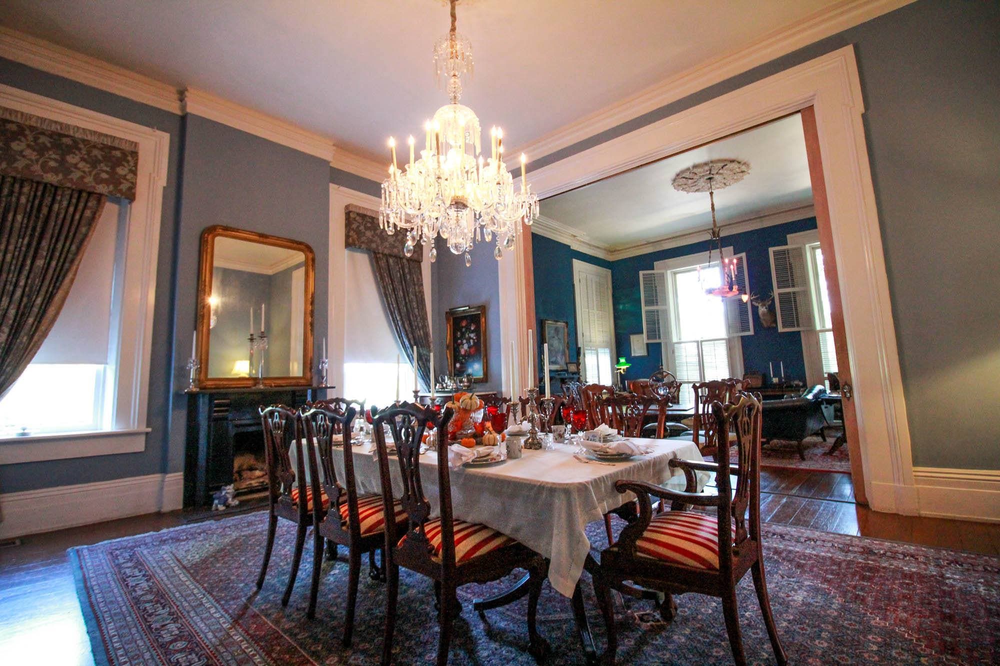 A spacious dining room with a chandelier, antique furniture, and a table set for a meal.